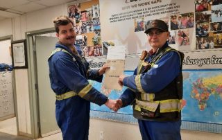 Cory receiving a Bouchier Foundational Award certificate in a workplace setting, shaking hands with a colleague in front of a safety-themed bulletin board.